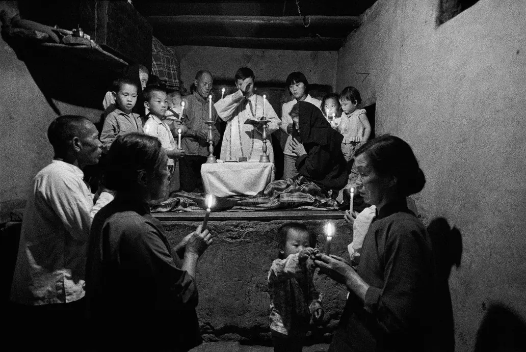 Lu Nan | Kelyje, Katalikų Bažnyčia Kinijoje. Kunigas teikia apeigas sergančiajam, prikaustytam prie lovos. Šaansi provincija, Kinija. 1992. © Lu Nan | Magnum Photos+
